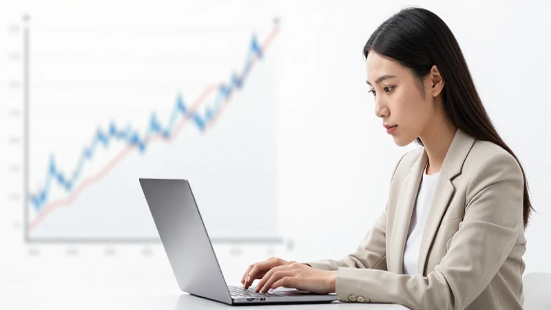 Mujer observa laptop con gráfico financiero